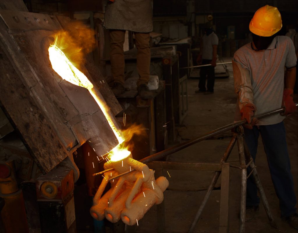 Operator pouring molten steel into sand moulds